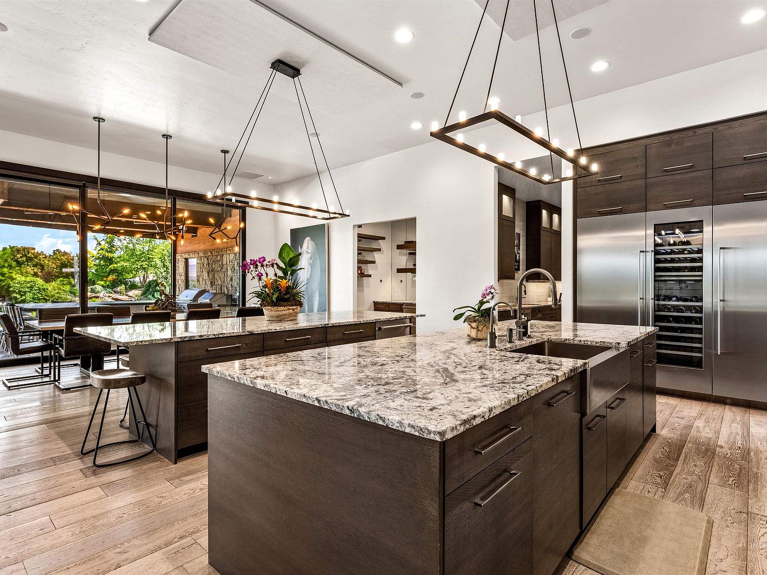 Chef's kitchen with two quartzite-topped islands, dark walnut cabinetry, a stainless apron sink, paneled refrigeration, and a glass-fronted wine column