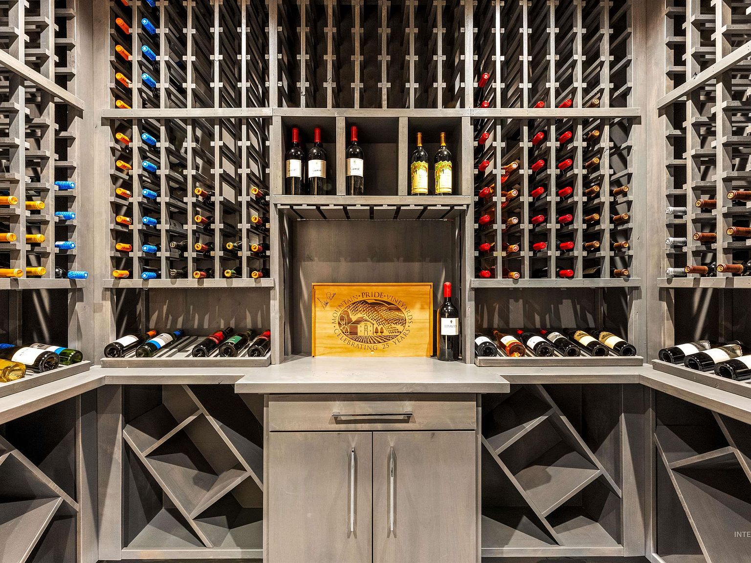 Climate-controlled wine cellar with floor-to-ceiling gray-stained racking filled with bottles and a center display shelf and counter
