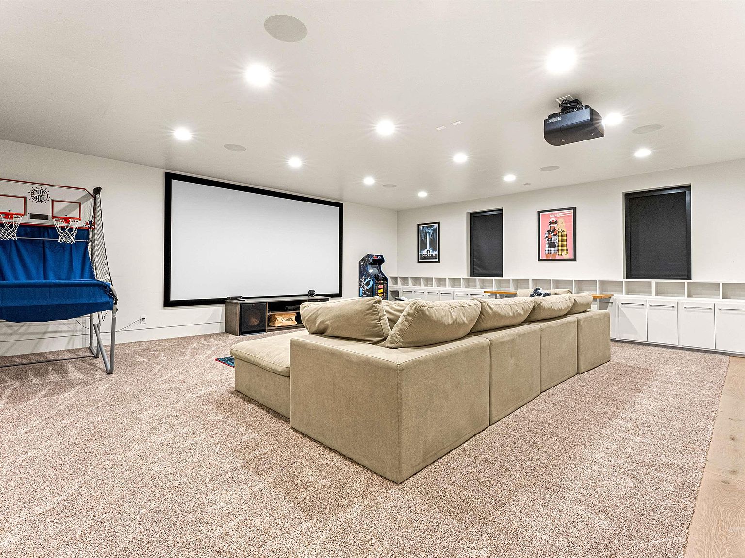 Bonus room and theater with a large projection screen, sectional sofa, ceiling-mounted projector, and a basketball arcade game in the corner